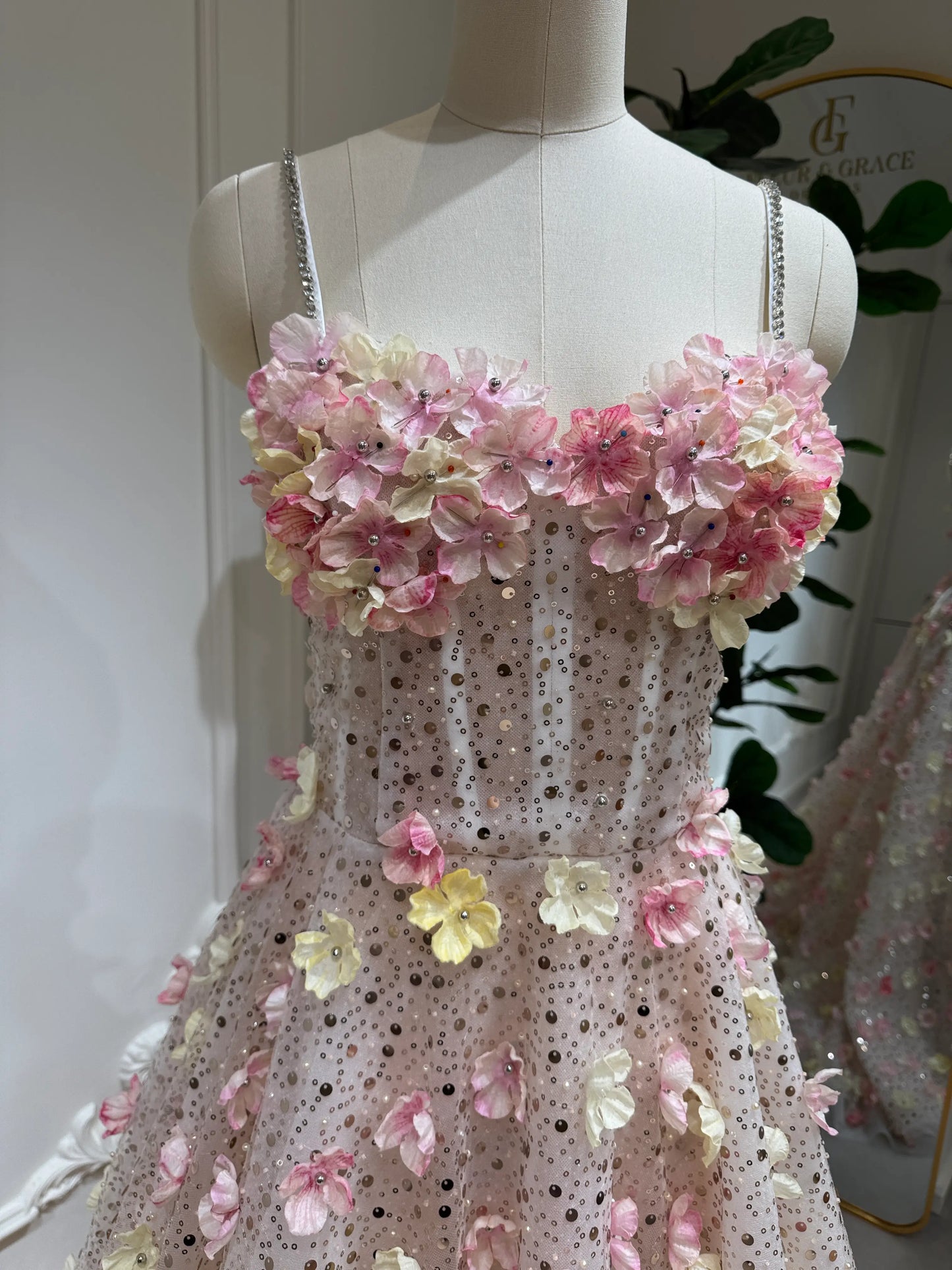 The Alice Gown FG018 is a dreamy, fairytale-inspired dress perfect for prom, photoshoots, and formal events. Crafted with exquisite beaded lace and adorned with delicate handmade 3D flowers in soft pink and yellow tones, this gown shimmers with every step. Featuring a romantic sweetheart neckline, lace‑up back for an adjustable fit, and thin stone‑accented straps, the Alice Gown blends fantasy with elegance. The regal court train adds a show‑stopping finish, making it ideal for prom nights, garden par