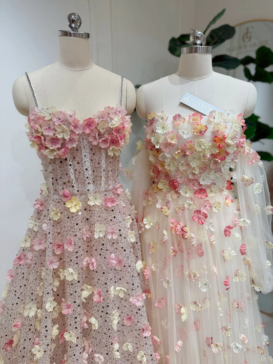 Two mannequins wearing pink and yellow 3D floral lace gowns with sweetheart necklines and shimmering beaded details.