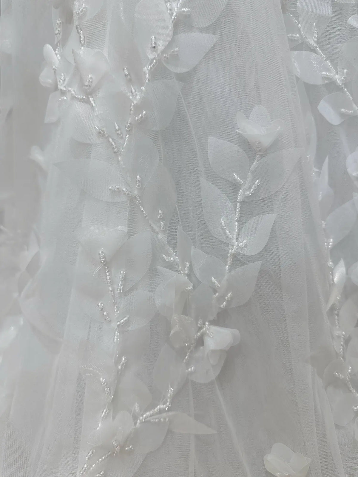 White tulle wedding dress fabric with delicate 3D floral leaf appliqués and intricate hand-sewn bead detailing.