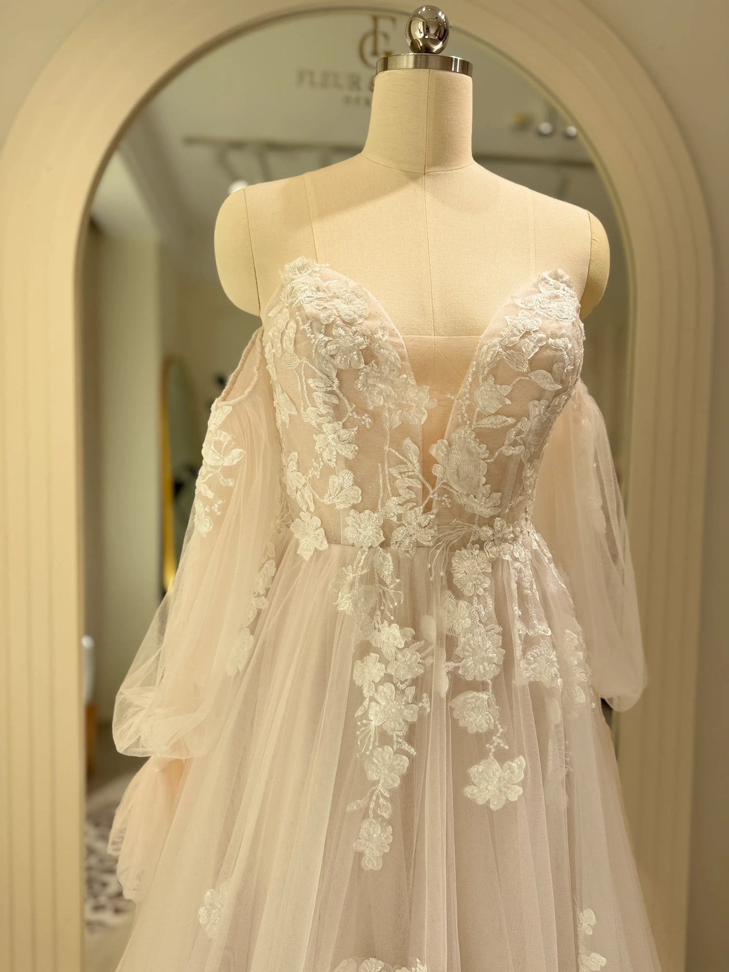 Aure Gown by Fleur&Grace Designs – romantic floral embroidered wedding dress with plunging neckline, removable long sleeves, soft tulle skirt, and A-line silhouette, perfect for whimsical weddings and elopements.