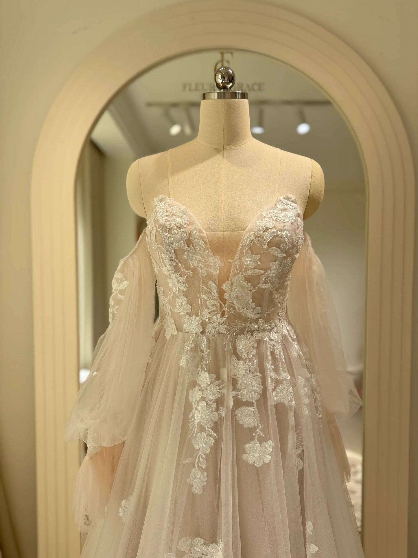 Aure Gown by Fleur&Grace Designs – romantic floral embroidered wedding dress with plunging neckline, removable long sleeves, soft tulle skirt, and A-line silhouette, perfect for whimsical weddings and elopements.
