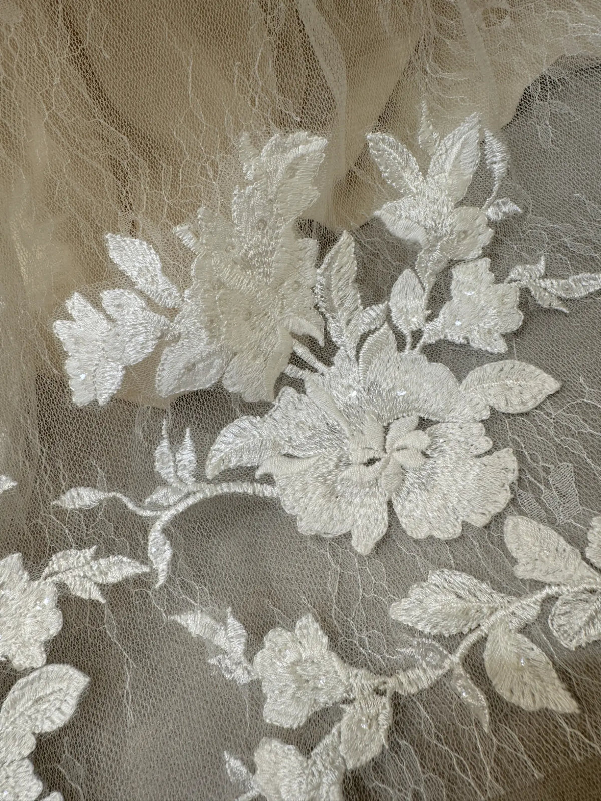 White floral embroidery with subtle sequins on delicate sheer tulle fabric for a wedding gown.