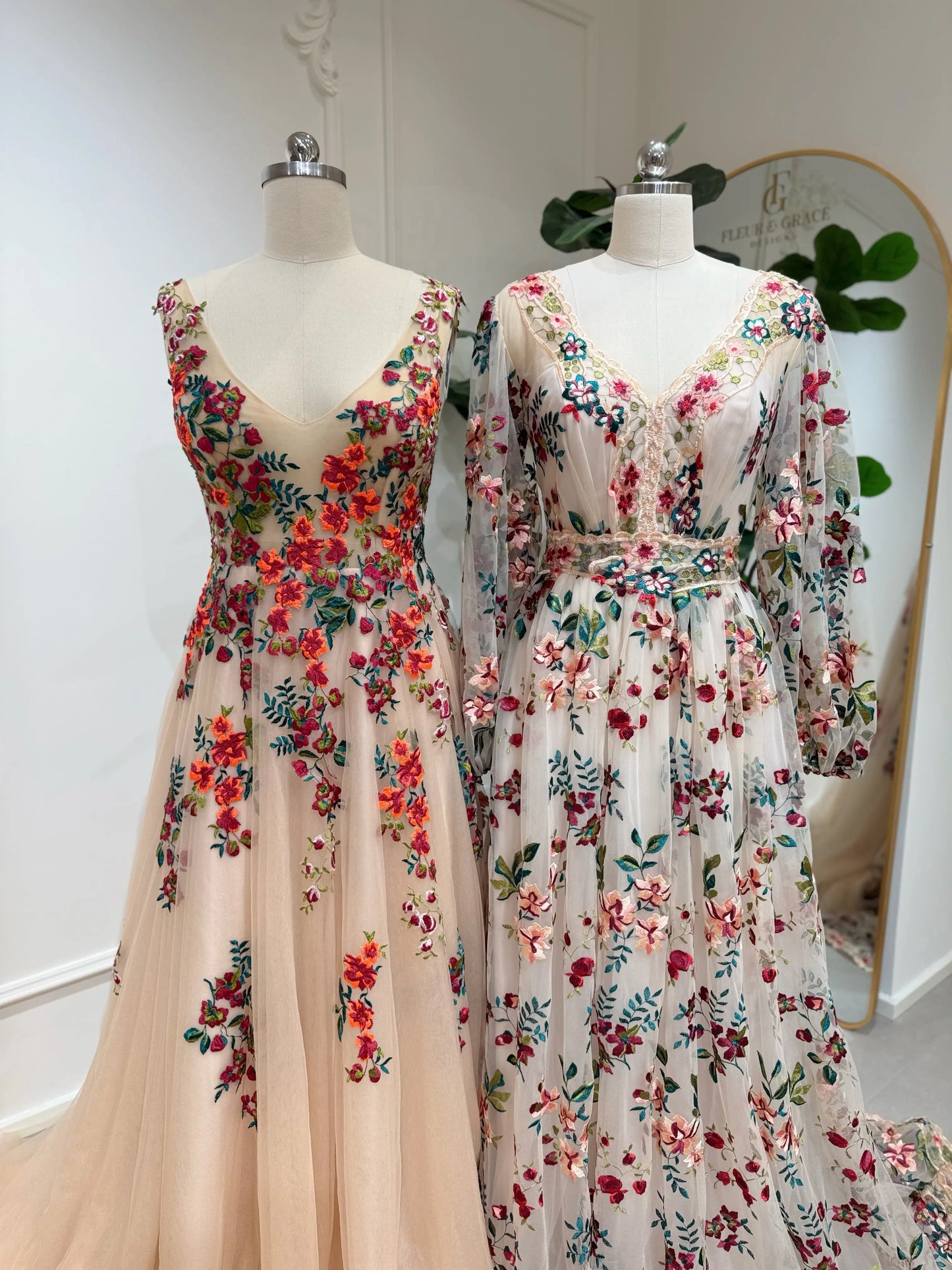 Bride mannequin wearing the Monica Gown by Fleur&Grace Designs — colorful wedding dress with orange floral appliqués, meadow green embroidery on champagne tulle, V-neck, sleeveless bodice, lace-up back, and pockets.