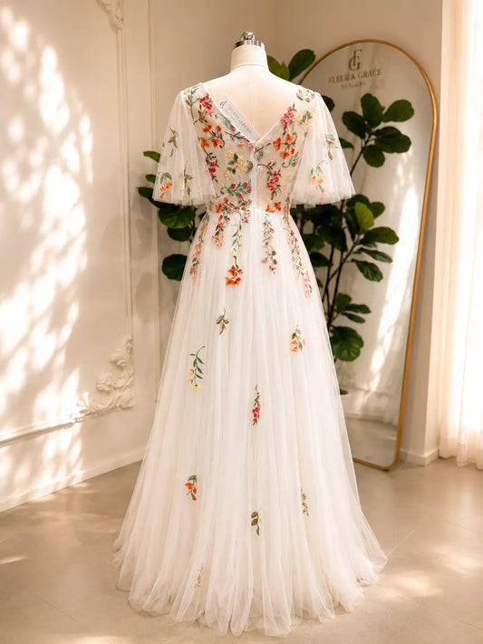 White A-line wedding dress with colorful floral embroidery, flutter sleeves, and a flowing tulle skirt on a mannequin.