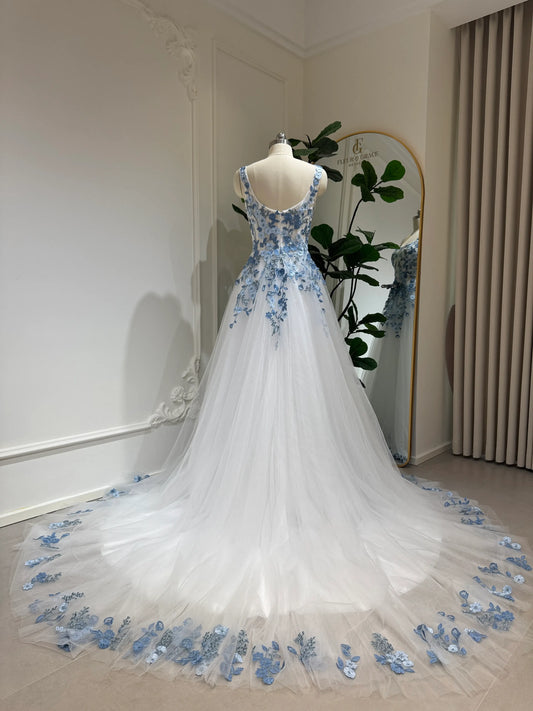 The Iris Gown by Fleur&Grace Designs is a graceful and romantic wedding dress adorned with elegant dusty blue floral embroidery. Crafted in soft tulle with a structured silhouette, this gown features a timeless square neckline, a comfortable built-in bodice, and pockets for modern functionality.