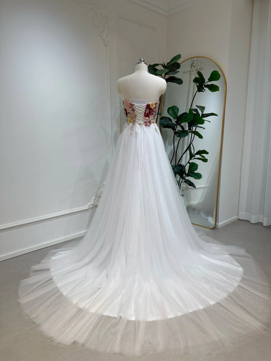 Model wearing the Julie Gown FG031 by Fleur&Grace Designs — strapless fairy wedding dress with a beaded colorful sequin floral bodice, lace-up back, and blush pink tulle skirt with chapel-length train.