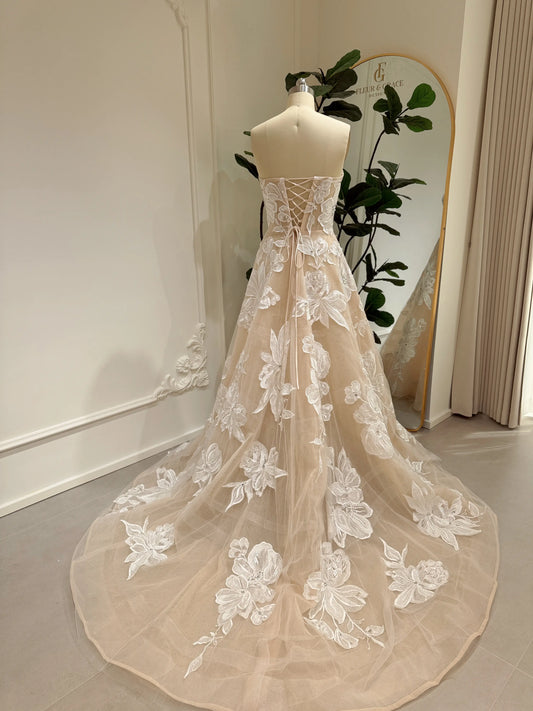 Mannequin wearing the Mira Gown FG024 by Fleur&Grace Designs — a strapless ivory tulle wedding dress with floral embroidery appliqués, handmade rhinestone embellishments, boned bodice, lace‑up back, sheer underlay, and a chapel‑length train.