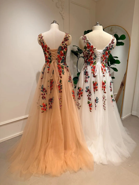Two Monica A-line wedding dresses in champagne and white with vibrant floral embroidery and lace-up corset backs.