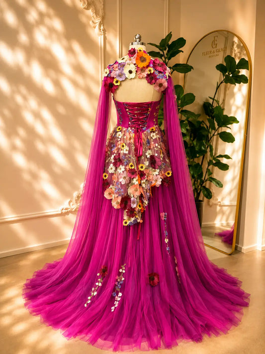 Magenta floral appliqué corset gown with detachable cape sleeves and a voluminous layered tulle skirt.