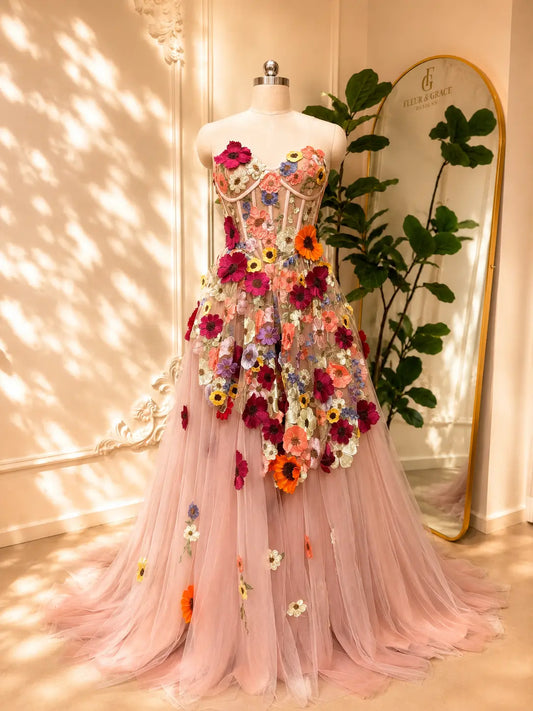 Blush pink tulle ball gown featuring a structured corset bodice and vibrant 3D floral appliqués for a romantic look.
