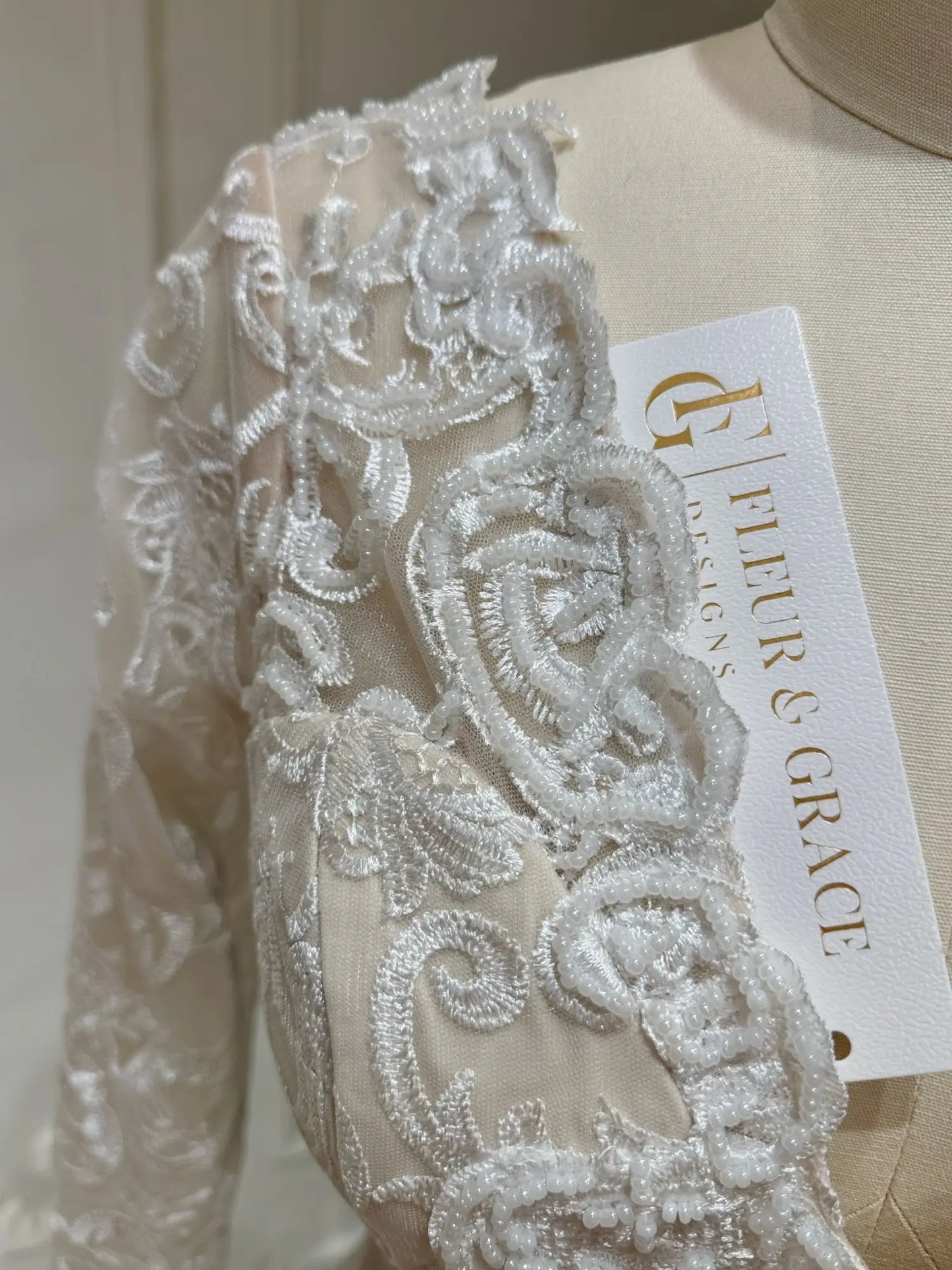 Close-up of Vera wedding dress featuring intricate white beaded lace embroidery over a soft nude illusion bodice.
