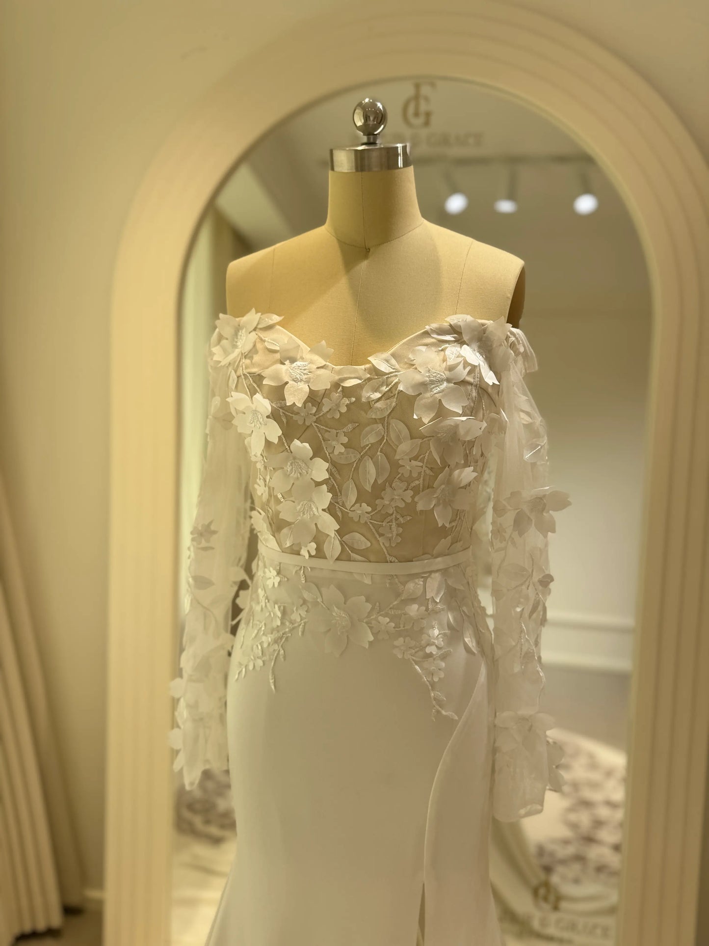 Zoe Gown by Fleur&Grace – minimalist matte crepe wedding dress with 3D floral lace bodice, long off-the-shoulder sleeves, side slit, and train, perfect for modern and romantic weddings.