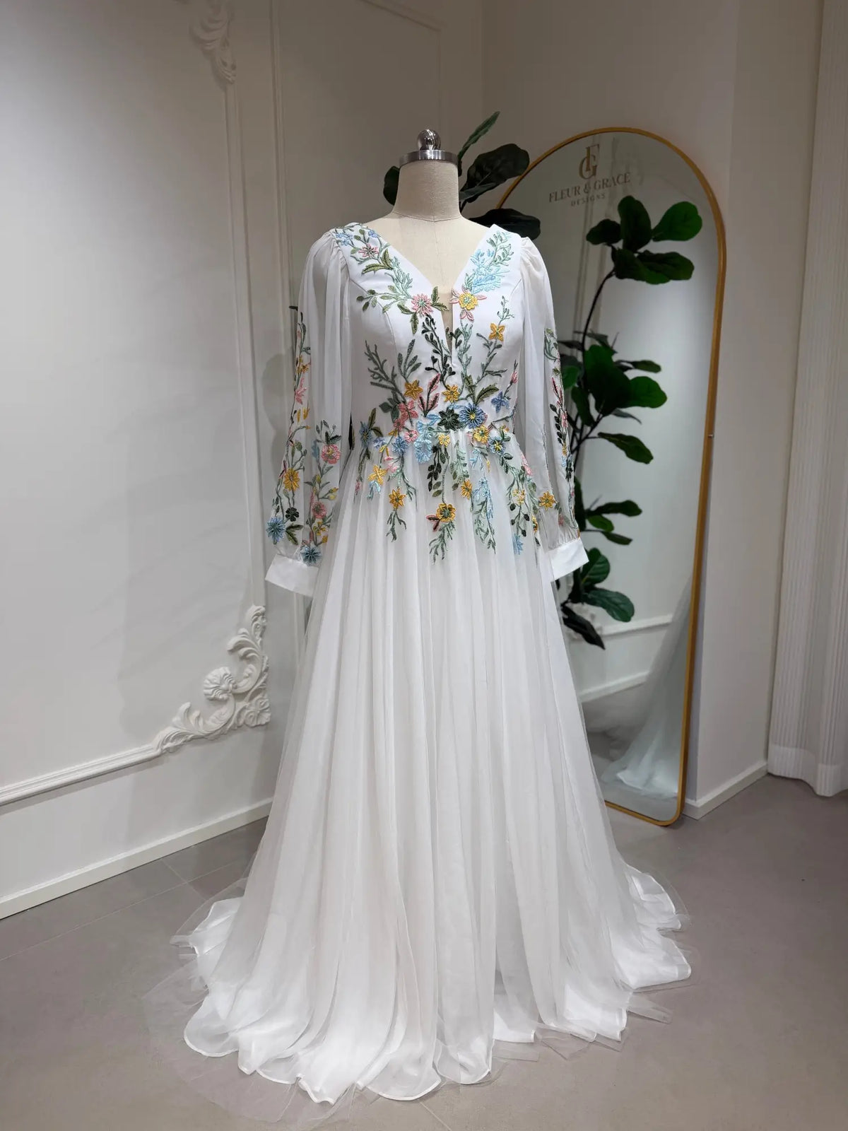 White A-line wedding dress featuring colorful floral embroidery, illusion long sleeves, and a V-neckline in airy tulle.