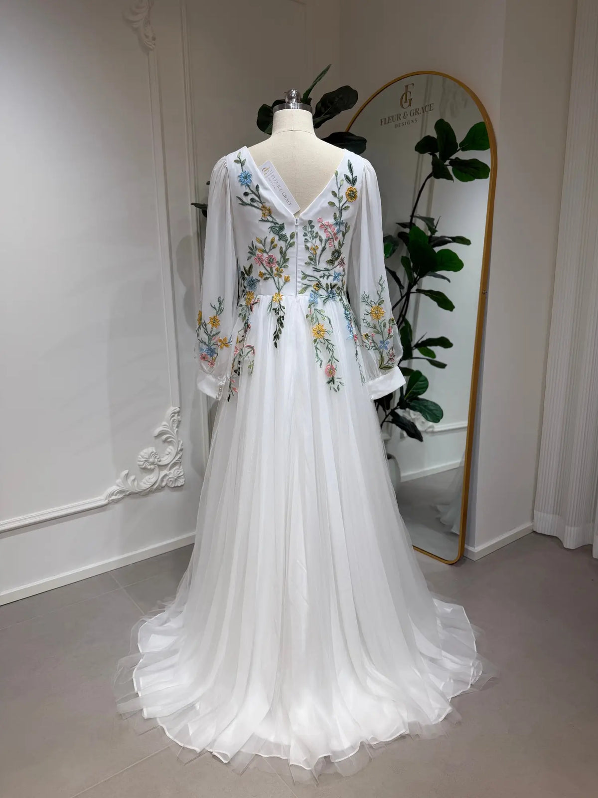 White A-line wedding dress with colorful floral embroidery, illusion long sleeves, and a V-back on a mannequin.