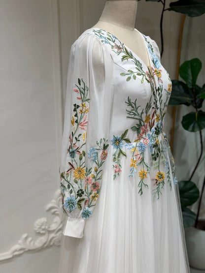White A-line wedding dress with long illusion sleeves and colorful pastel floral embroidery on tulle and chiffon.