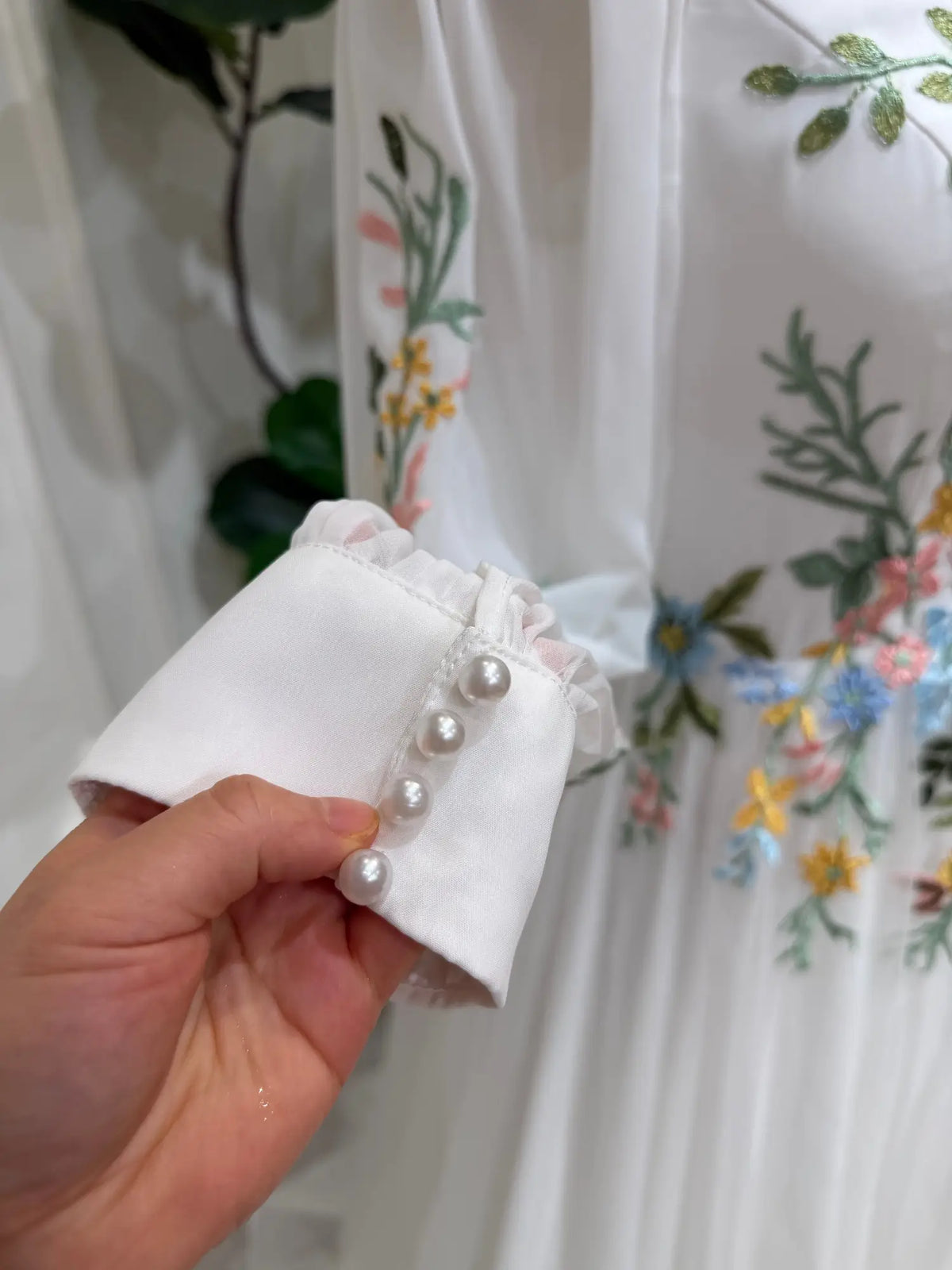 White wedding dress sleeve with colorful floral embroidery and pearl button cuff detail on airy tulle fabric.