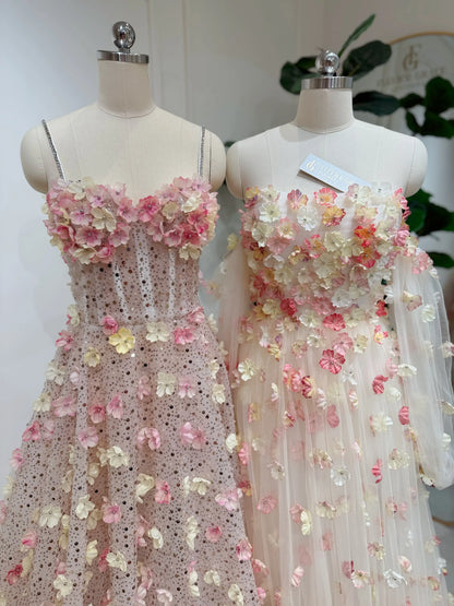 Two mannequins wearing pink and yellow 3D floral lace gowns with sweetheart necklines and shimmering beaded details.