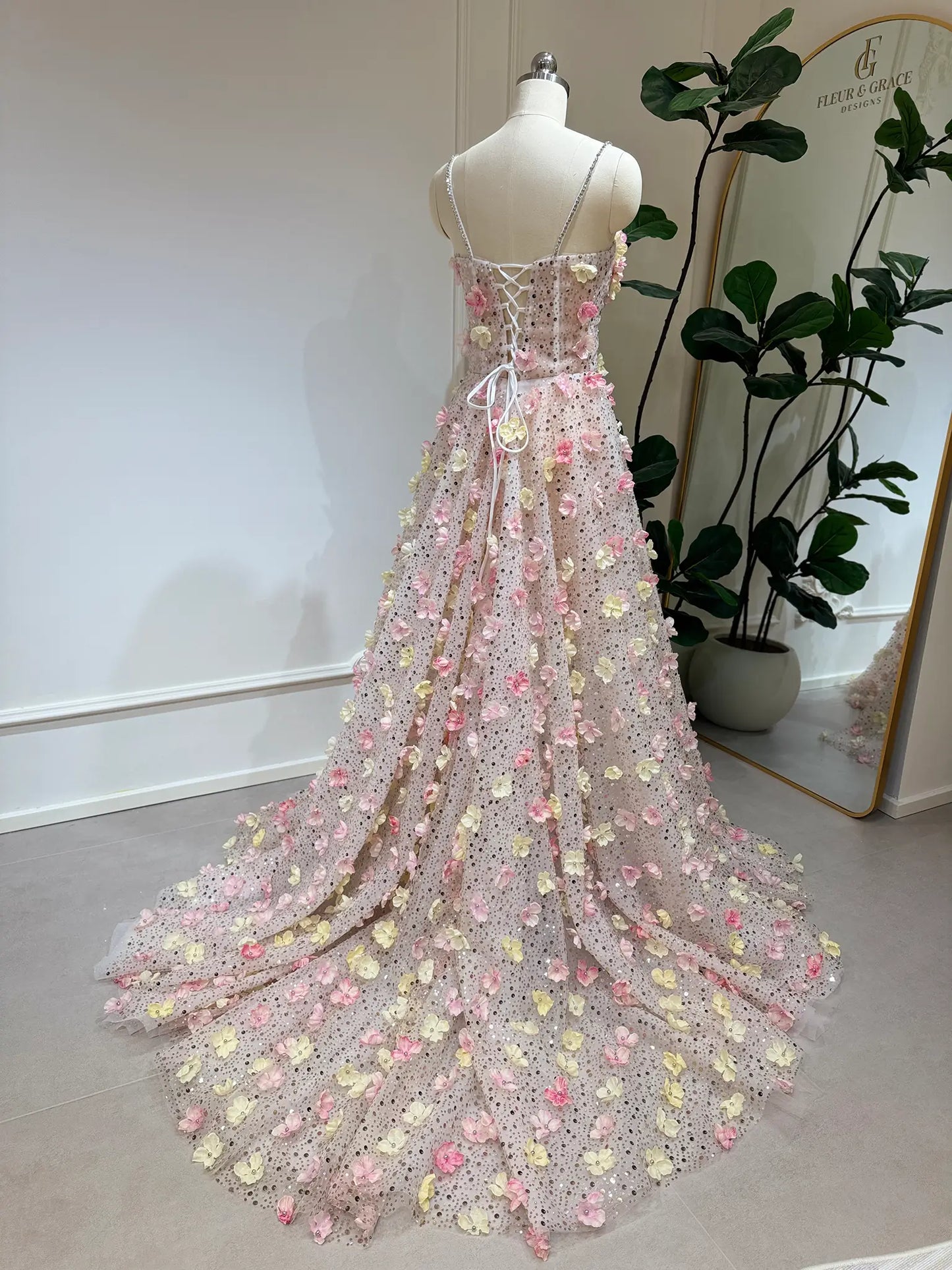Pink and yellow 3D floral lace gown with a lace-up back, stone-accented straps, and a flowing court train on a mannequin.