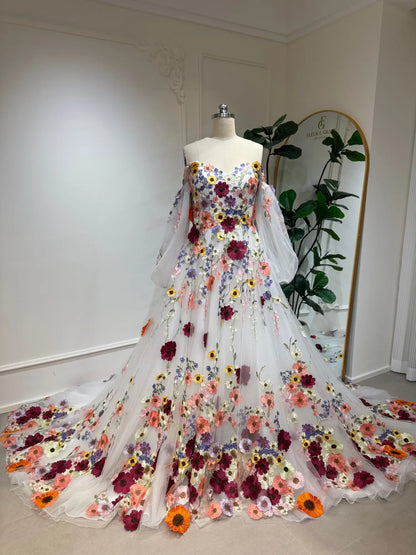 Off-the-shoulder A-line wedding dress with colorful 3D floral appliqués and sheer illusion bishop sleeves on a mannequin.