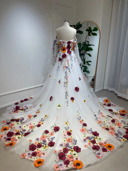 Off-the-shoulder wedding dress with colorful 3D floral appliqués and a sparkling tulle A-line skirt on a mannequin.
