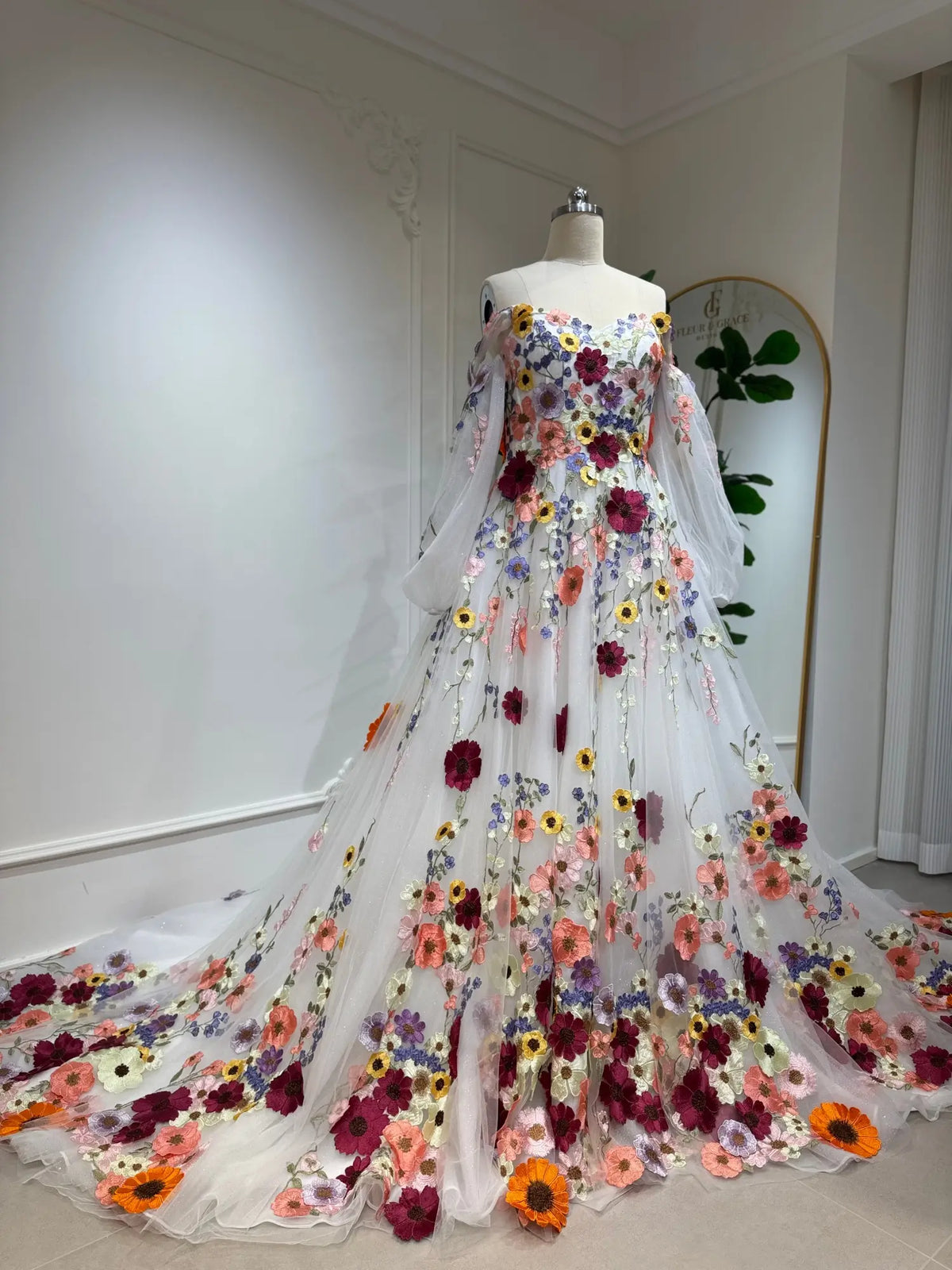 A-line wedding dress with 3D colorful floral appliqués, off-the-shoulder neckline, and sheer bishop sleeves on a mannequin.