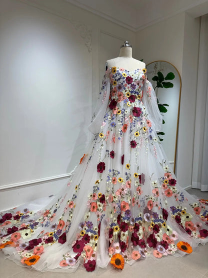 A-line wedding dress with 3D colorful floral appliqués, off-the-shoulder neckline, and sheer bishop sleeves on a mannequin.