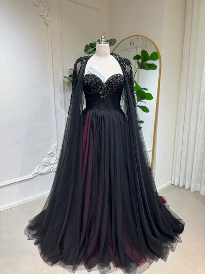 Black and burgundy A-line wedding dress with a beaded corset bodice and detachable illusion cape on a mannequin.