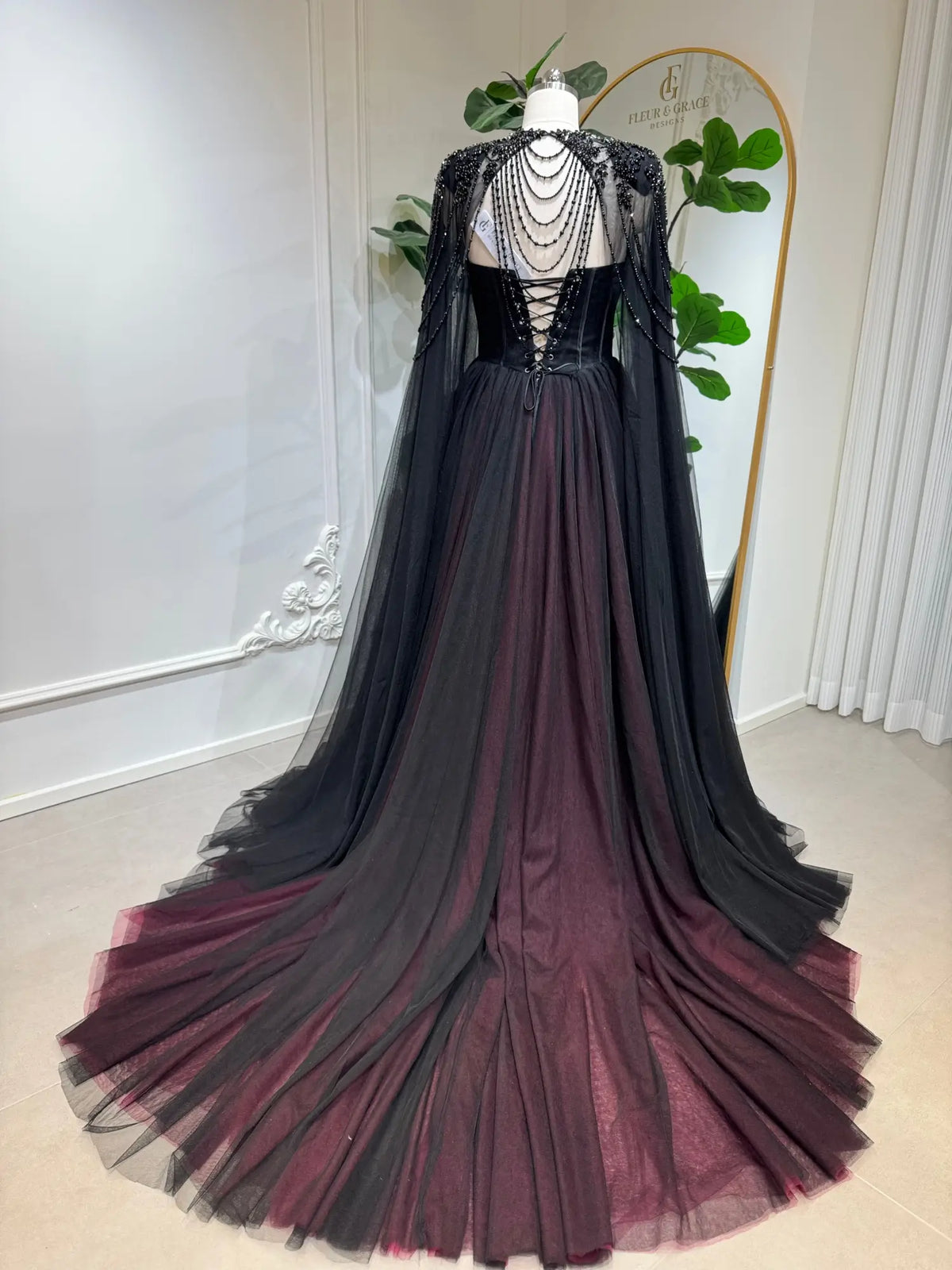 Black and burgundy tulle wedding dress with a beaded corset back, lace-up closure, and a dramatic detachable illusion cape.