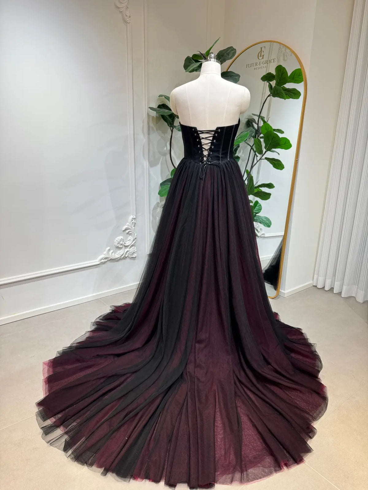 Black and burgundy tulle wedding dress with a strapless corset bodice and lace-up back on a mannequin.