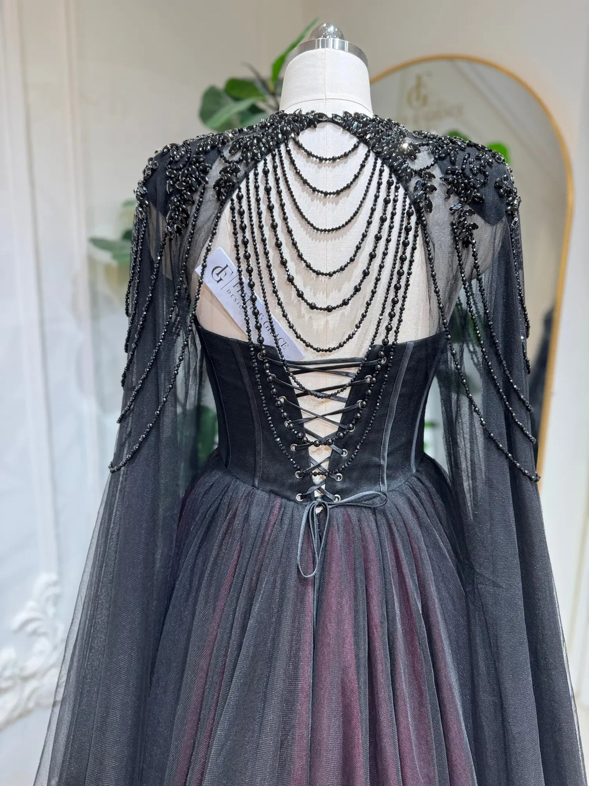 Black and burgundy tulle wedding dress with a beaded corset back, lace-up closure, and a detachable illusion cape.