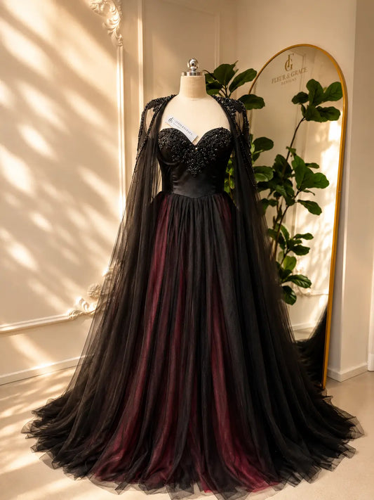 Black and burgundy tulle wedding dress with a beaded corset bodice and detachable illusion cape on a mannequin.