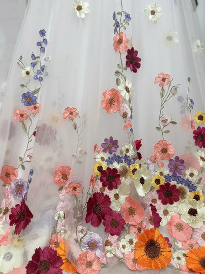 Off-white tulle wedding dress fabric featuring vibrant multicolored floral embroidery in pink, orange, and purple.