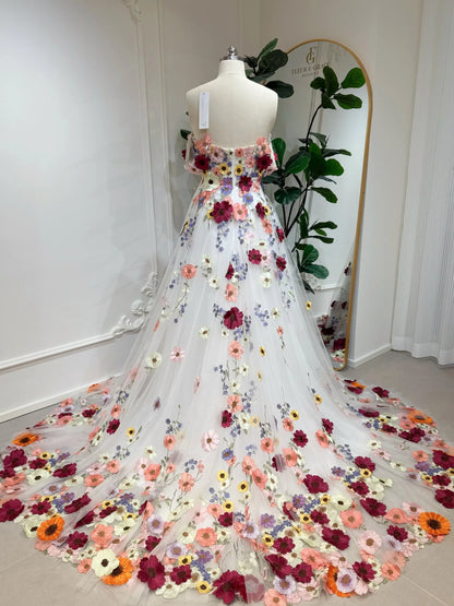 Off-the-shoulder tulle wedding gown featuring colorful floral embroidery and a chapel-length train on a mannequin.