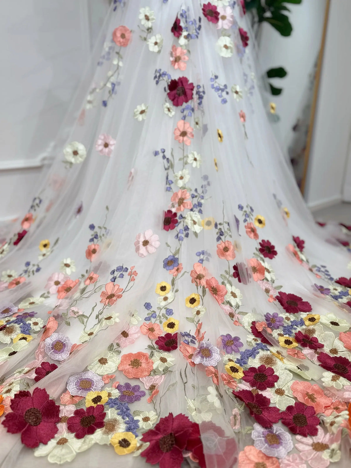 Off-white tulle wedding gown with vibrant multicolored floral embroidery and a flowing chapel-length train.