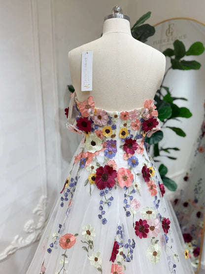 Off-the-shoulder wedding gown in white tulle with vibrant multicolored floral embroidery on a dress form.