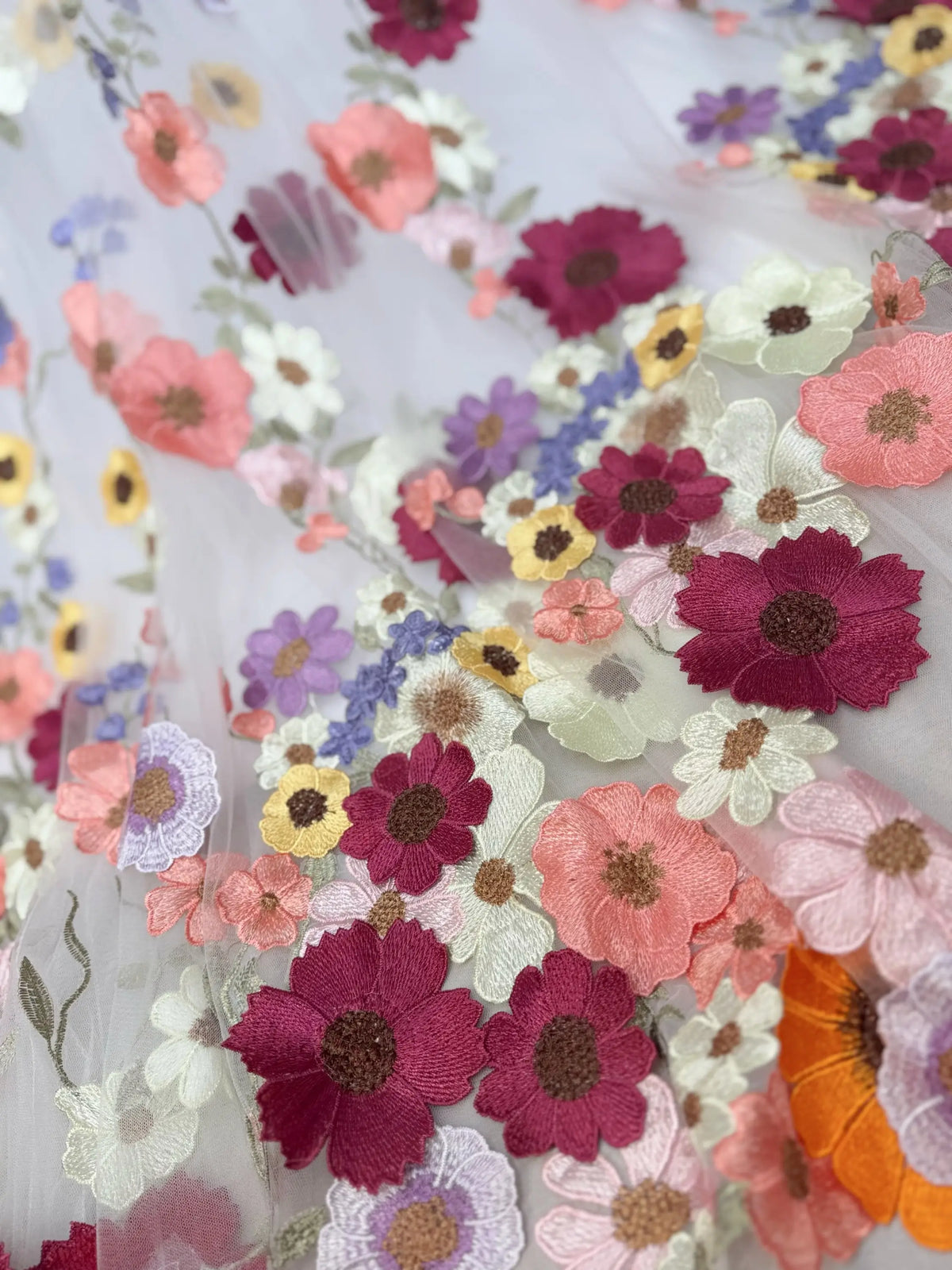 Off-white tulle fabric featuring vibrant, multicolored floral embroidery appliqués for a whimsical wedding gown.