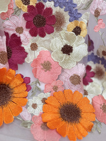 Close-up of off-white tulle wedding dress fabric with vibrant, multicolored floral embroidery appliqués.