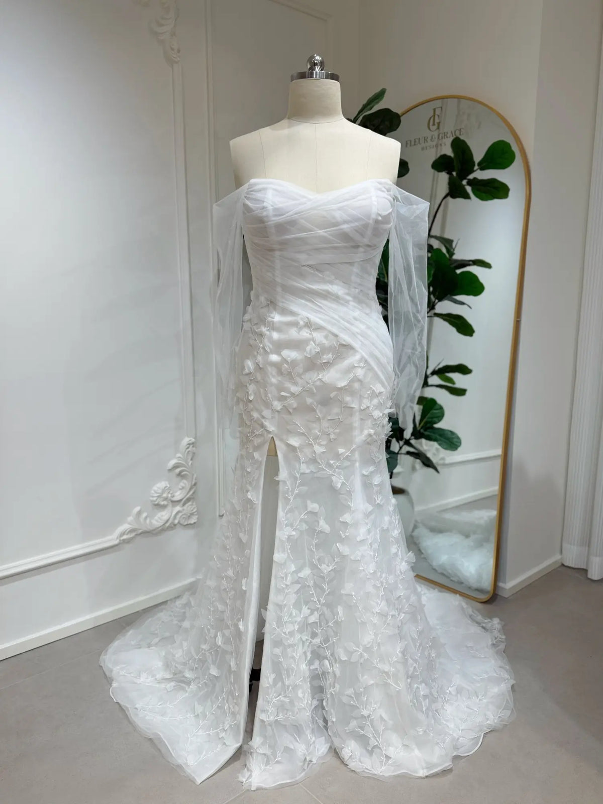 White mermaid wedding dress with 3D floral appliqués, off-the-shoulder illusion sleeves, and a front leg slit.