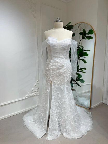 White mermaid wedding dress with 3D floral appliqués, off-the-shoulder illusion sleeves, and a front leg slit.
