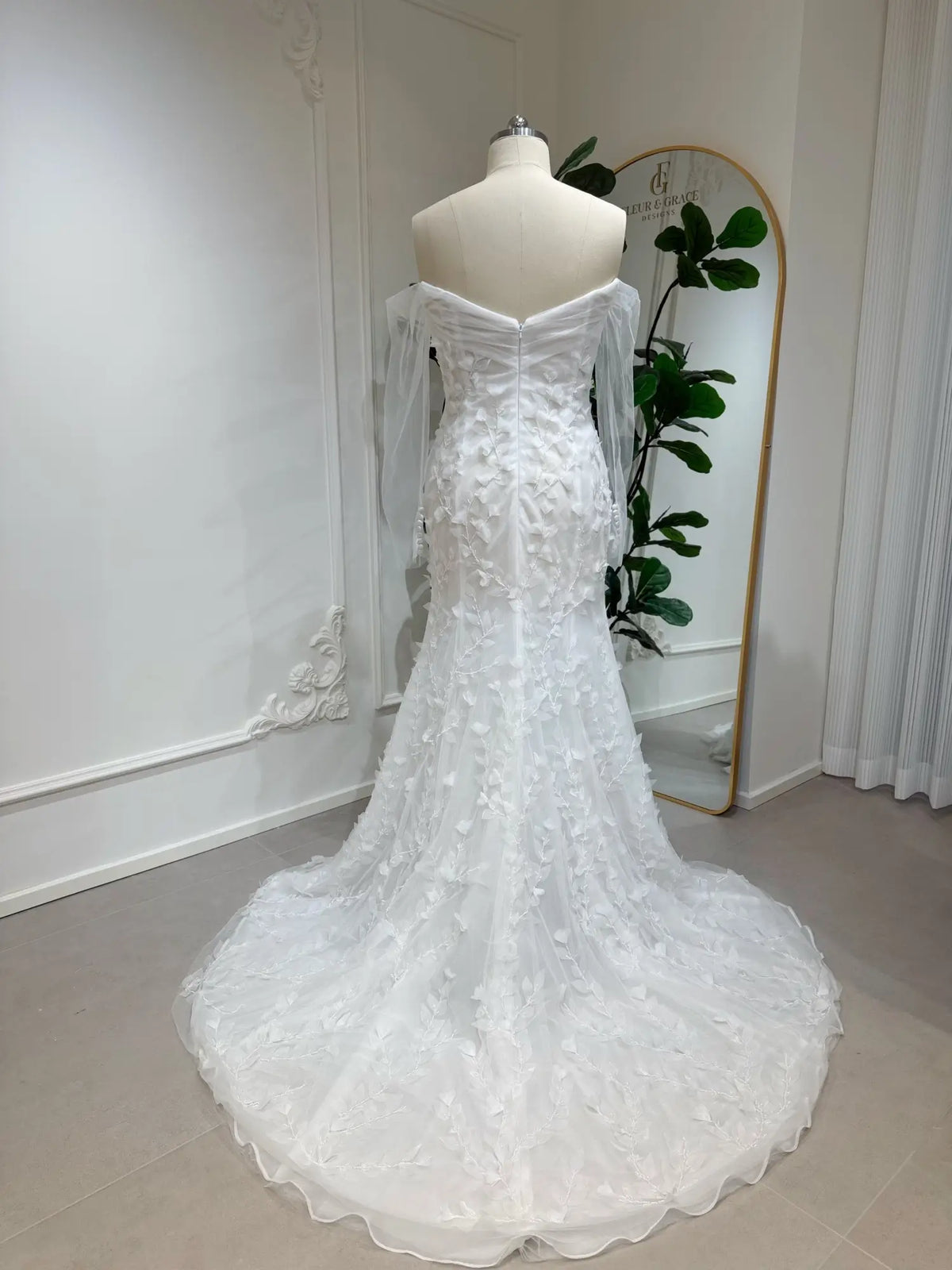 White mermaid wedding dress with 3D floral appliqués, off-the-shoulder illusion sleeves, and a flowing train.