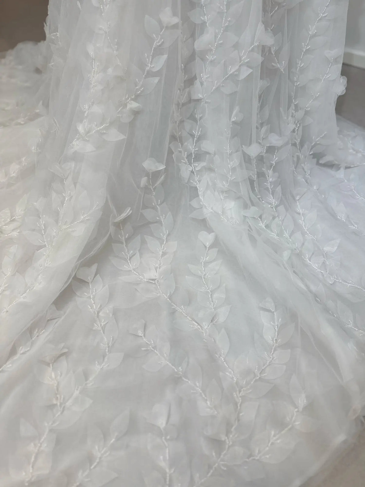 White tulle wedding dress fabric featuring delicate 3D leaf appliqués and intricate hand-sewn beading detail.