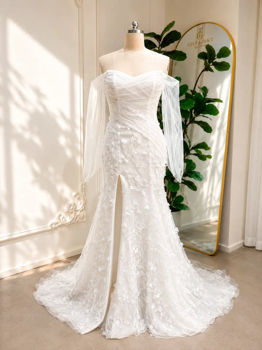 White mermaid wedding dress with 3D floral appliqués, off-the-shoulder illusion sleeves, and a front leg slit.