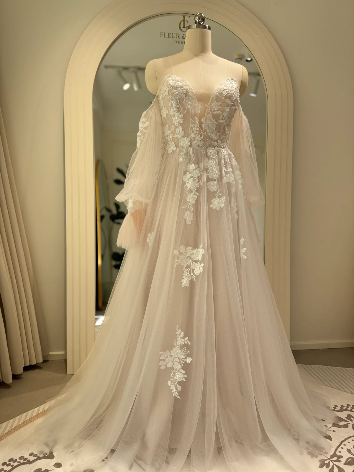 Ivory tulle wedding gown with floral embroidery, plunging illusion neckline, and removable sheer puff sleeves on a mannequin.