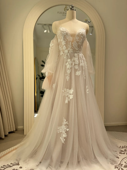 Ivory tulle wedding gown with floral embroidery, plunging illusion neckline, and removable sheer puff sleeves on a mannequin.
