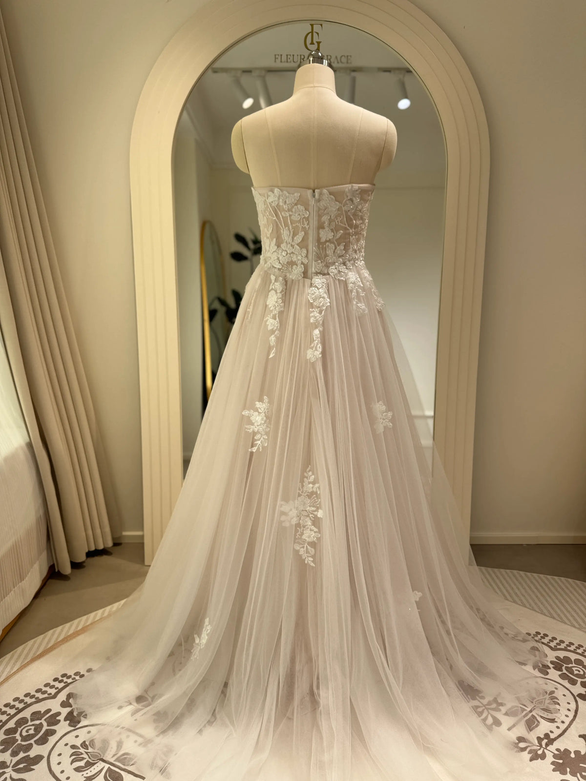 Back view of an ivory A-line wedding gown with floral embroidery on tulle, a strapless bodice, and a soft sweep train.