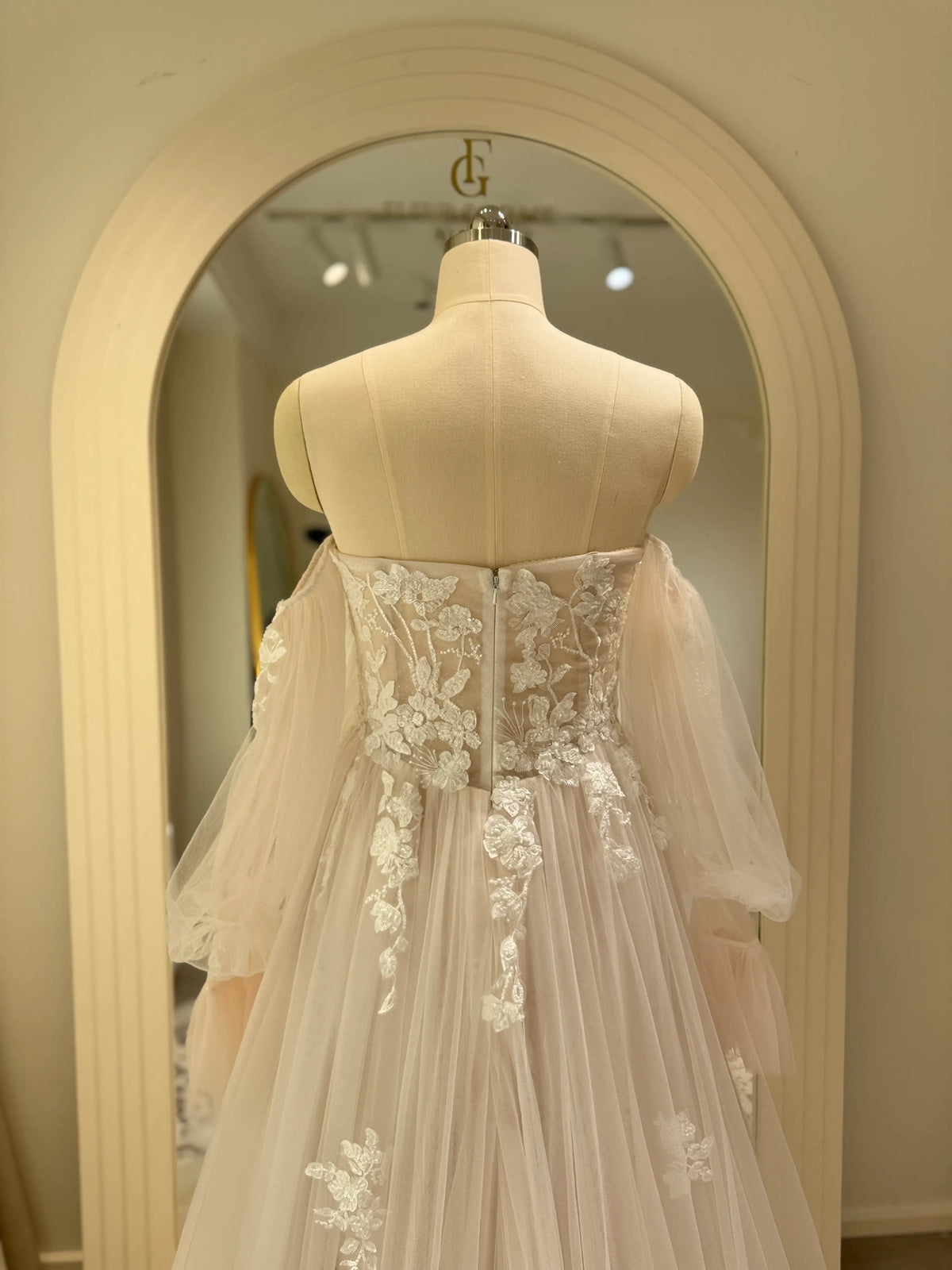 Ivory tulle wedding gown with floral embroidery, structured bodice, and removable sheer puff sleeves on a mannequin.