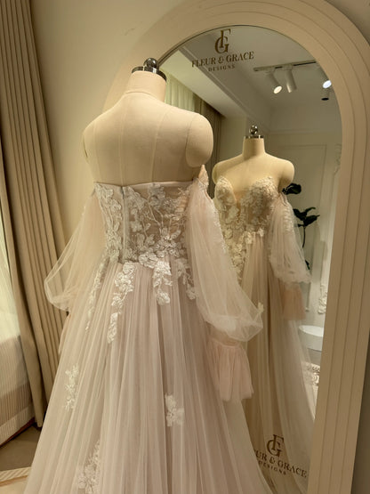 Ivory tulle wedding gown with floral embroidery, plunging V-neck, and removable long puff sleeves on a mannequin.