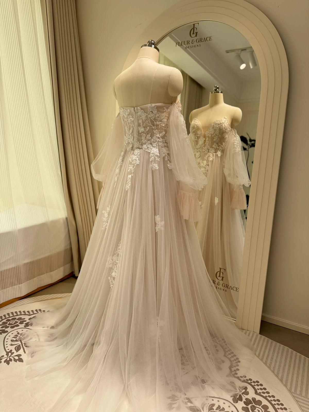 Ivory tulle wedding gown with floral embroidery, plunging neckline, and removable puff sleeves on a mannequin.