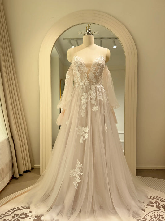 Ivory tulle wedding gown with floral embroidery, plunging V-neckline, and removable long puff sleeves on a mannequin.