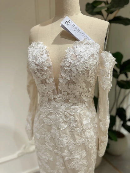 White mermaid wedding dress with floral embroidery, off-the-shoulder long sleeves, and a plunging sweetheart neckline.
